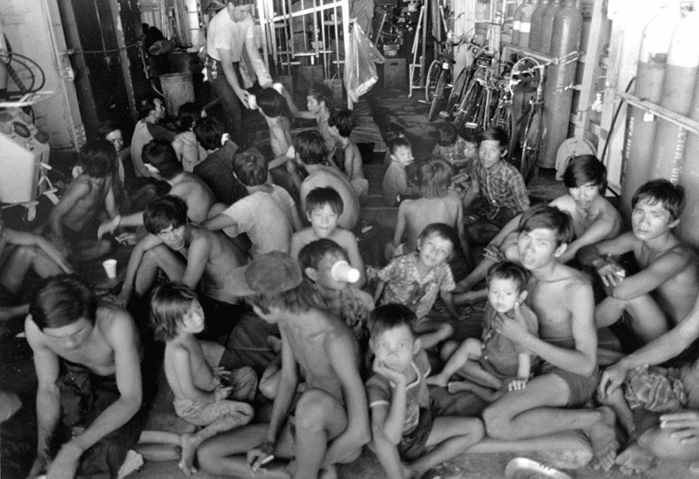 Des réfugiés vietnamiens à moitié nus, principalement des garçons, sont assis sur le sol après avoir été secourus.