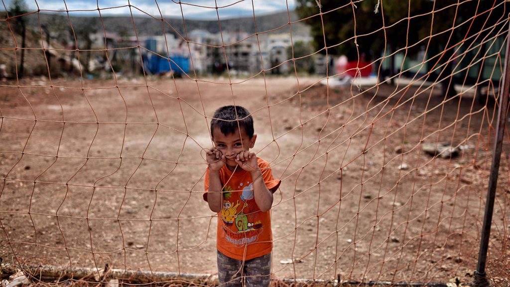 Un garçon regarde au loin, derrière un filet, au camp de réfugiés de Schisto à Athènes, en Grèce, le 8 juin 2016.